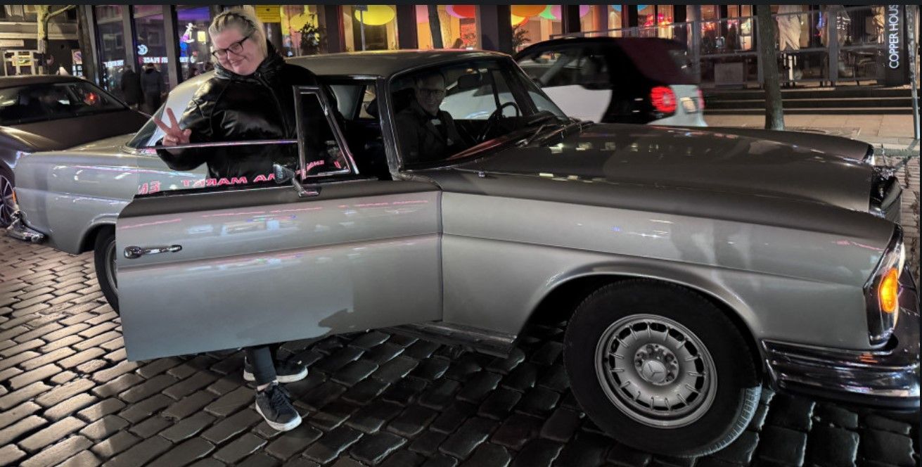 Susa am geöffneten Oldtimer auf einer nächtlichen Kiezstraße